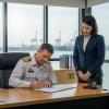 A ship's captain, looking serious and professional, signing a document at a wooden desk in a well-lit office